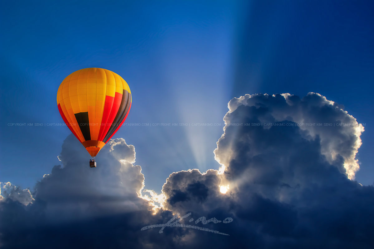 Hot Air Balloon High in Cloudy Blue Sky with Sunrays
